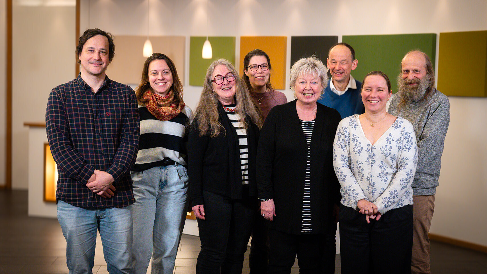 Gruppenbild. Die Personen stehen nebeneinander und leicht versetzt hintereinander. Sie blicken freundlich und lachend in Richtung Kamera.