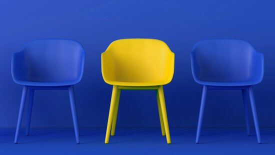 Ein gelber und zwei blaue Stühle vor blauer Wand