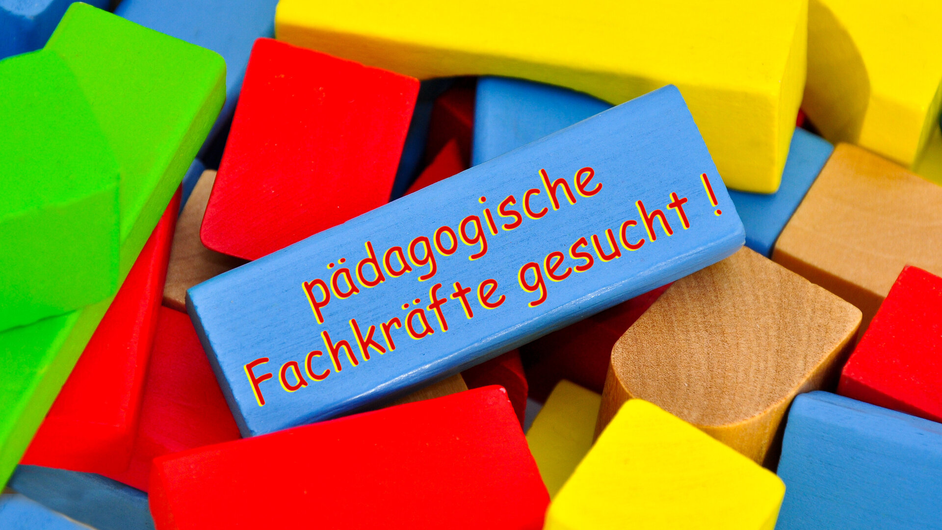 Bunte Bauklötze liegen aufeinander gestapelt. Einer der Klötze trägt die Aufschrift "Pägagogische Fachkräfte gesucht!"